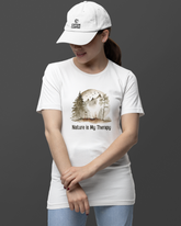 Person wearing a white t-shirt with a nature-themed design and a cap on a dark background